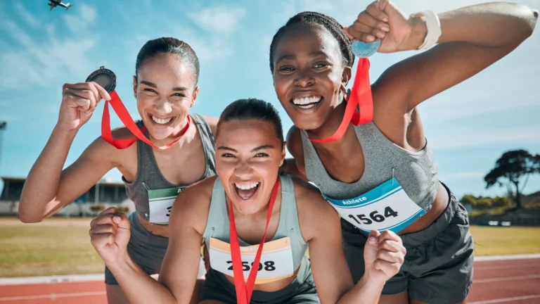 Three athletic women proudly wearing medals, celebrating strength, confidence, and pelvic wellbeing for athletic women.