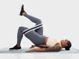 Woman performing glute bridge exercise with resistance band to strengthen hips and support pelvic foundation support for athletes.